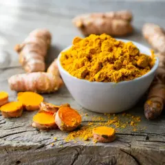 Kurkuma-Wurzeln und Pulver auf Holz. Informiert über die Frage: wieviel curcumin pro tag.