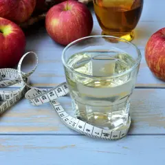 Ein Glas Apfelessig, Äpfel und ein Maßband. Ein täglicher Apfelessig-Schluck für die Gesundheit und eine schlanke Linie.