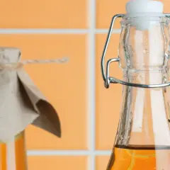 Zwei Flaschen mit bernsteinfarbener Flüssigkeit, eine mit Bügelverschluss, die andere mit Papier und Schnur abgedeckt. Essig oder Essigessenz für die Küche.