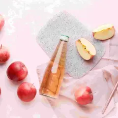 Frische Äpfel und eine Flasche mit Apfelessig mit Wasser. Ein Löffel liegt daneben.