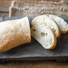Ein rustikales ciabatta mit sauerteig, aufgeschnitten auf einem Holzbrett.