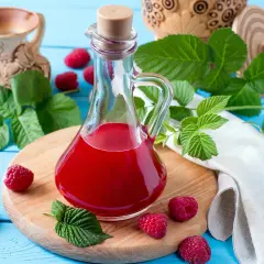 Flasche mit rotem Himbeeressig, frischen Himbeeren und Blättern. Perfekt, um Himbeeressig selber machen.