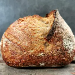 Ein rustikales Brot mit knuspriger Kruste und luftiger brot krume liegt auf Holzbrettern.