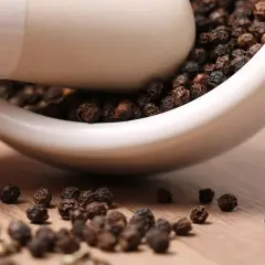Schwarze Pfefferkörner in einem Mörser. Sie stammen ursprünglich aus Indien und sind ein beliebtes Gewürz.