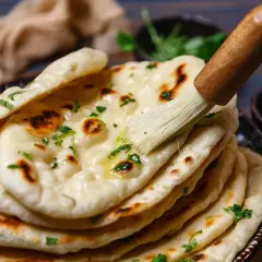 Frisch gebackenes Naan Brot, mit Butter bestrichen und mit Kräutern garniert, bereit zum Servieren aus der Pfanne.