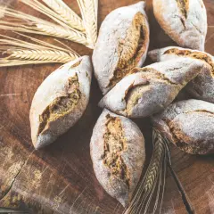 Frische Brötchen, gebacken aus verschiedenen Getreidearten, liegen auf einem rustikalen Holzbrett, umgeben von Ähren.
