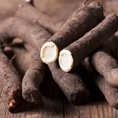 Frisch geerntete Schwarzwurzeln liegen auf Holz. Das Innere einer aufgeschnittenen Wurzel zeigt das helle Fruchtfleisch. Perfekt, um Schwarzwurzel anzubauen.