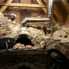 Frisches Brot wird im Pizzaofen gebacken. Mehrere Laibe liegen bereit, einige sind schon im Ofen.