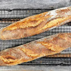 Zwei knusprige, goldbraune Sauerteig Baguettes liegen auf einem schwarzen Gitterrost.