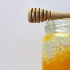 Ein Holzlöffel ruht auf einem Glas mit honig kristallisiert. Die Kristalle bilden eine interessante Textur.