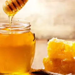Ein Honigheber tropft goldenen Manuka Honig in ein Glas. Daneben liegt ein Stück Wabe. So schmeckt manuka honig!