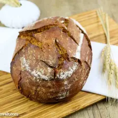 Ein rustikales Bierbrot mit Sauerteig, auf einem Holzbrett mit einem weißen Tuch und Ähren dekoriert.