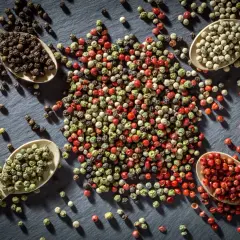 Vier Löffel mit verschiedenen Pfefferkörnern: schwarz, weiß, grün und rot. Sie zeigen den vielfältigen **Pfeffer Ursprung** und seine Farben.