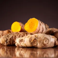 Ein Haufen frischer Kurkumawurzeln, eine davon aufgeschnitten, enthüllt ihr leuchtend orangefarbenes Inneres. Die Wurzeln stammen aus tropischen Regionen und sind bekannt für ihre gesundheitlichen Vorteile.