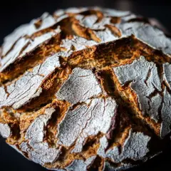 Ein rustikales Roggenmischbrot mit Sauerteig, dessen Kruste mit Mehl bestäubt ist und tiefe Rillen aufweist.