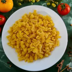 Ein Teller mit gedrehten Nudeln, die aus Hartweizengrieß hergestellt sind, umgeben von frischen Tomaten und Gewürzen.
