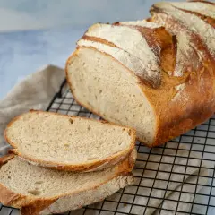 Frisch gebackenes Brot, perfekt zum Brot backen mit Hefe. Zwei Scheiben liegen auf einem Gitter, daneben ein Laib mit knuspriger Kruste.
