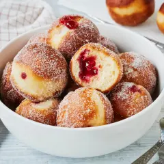 Schüssel voller süßer Berliner, bestreut mit Zucker. Ein Berliner ist aufgeschnitten und zeigt die rote Marmeladenfüllung. Perfekt für den Karneval!
