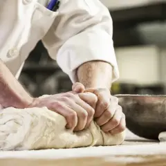 Hände kneten kräftig Brotteig. Die Frage "wie lange brotteig kneten" beschäftigt Bäcker, um das perfekte Ergebnis zu erzielen.