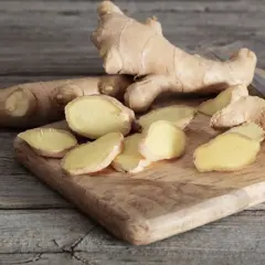 Frischer Ingwer, teils in Scheiben geschnitten, liegt auf einem Holzbrett. Der Unterschied zwischen ganzen Wurzeln und den Scheiben ist deutlich zu erkennen.