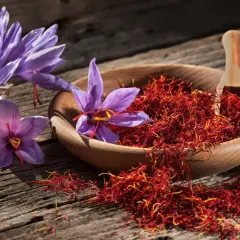 Safranfäden in einer Holzschale und lila Krokusblüten auf rustikalem Holz. Die **Safran Wirkung Gehirn** ist faszinierend, da das Gewürz für seine stimmungsaufhellenden Eigenschaften bekannt ist.