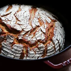 Frisch gebackenes Dinkel Mischbrot mit knuspriger Kruste und weißer Mehlschicht in einem roten Gusseisentopf.