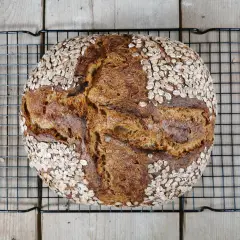 Ein rustikales Porridge Brot mit Haferflockenkruste, das auf einem Gitterrost abkühlt.