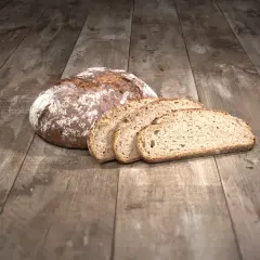 Ein Laib Brot liegt auf einem Holztisch, daneben vier Scheiben. Die ideale Kerntemperatur Brot ist erreicht.