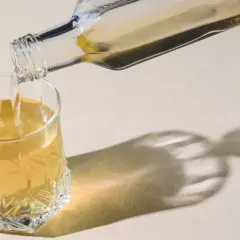 Klarer Flüssigkeit wird aus einer Glasflasche in ein Glas gegossen. Ein gesunder Schluck Essigwasser für den Tag.