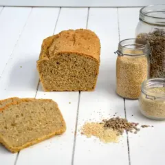 Brotlaib und Scheiben, daneben Gläser mit Quinoa, Sonnenblumenkernen und Sesam. Alles Zutaten für ein gesundes glutenfreies Mehl.
