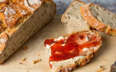 Frisch aufgebackenes Brot mit Butter und Marmelade auf einem Holzbrett. Ein Messer liegt daneben.