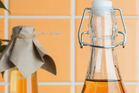 Zwei Flaschen mit bernsteinfarbener Flüssigkeit, eine mit Bügelverschluss, die andere mit Papier und Schnur abgedeckt. Essig oder Essigessenz für die Küche.
