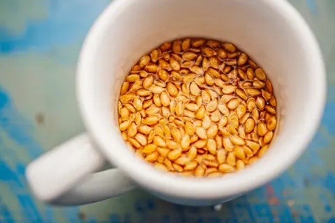 Eine weiße Tasse gefüllt mit goldenen Leinsamen, die in Wasser quellen. Ein gesundes Frühstück, das wie ein kleines Ei aussieht.