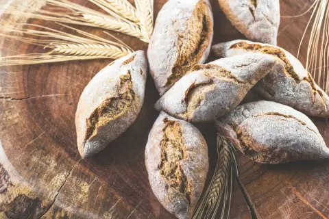 Frische Brötchen, gebacken aus verschiedenen Getreidearten, liegen auf einem rustikalen Holzbrett, umgeben von Ähren.