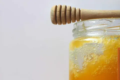 Ein Holzlöffel ruht auf einem Glas mit honig kristallisiert. Die Kristalle bilden eine interessante Textur.