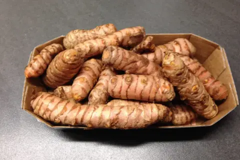 Frische Kurkuma-Wurzeln in einer Pappschale, bereit für leckere Kurkuma-Wurzel-Rezepte.