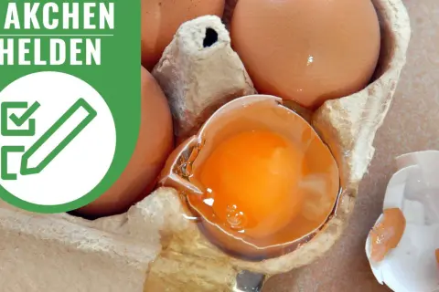 Braune Eier in einem Karton, ein Ei ist zerbrochen und zeigt das leuchtend orangefarbene Eigelb. Die Aufschrift "ÄKCHEN HELDEN" und ein Symbol mit einem Haken und Stift deuten auf die richtige Lagerung von Eiern hin.