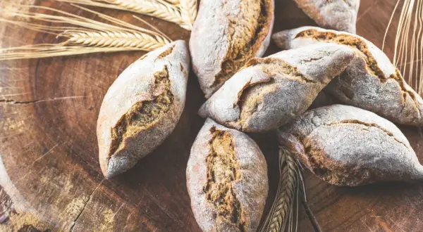 Frische Brötchen, gebacken aus verschiedenen Getreidearten, liegen auf einem rustikalen Holzbrett, umgeben von Ähren.
