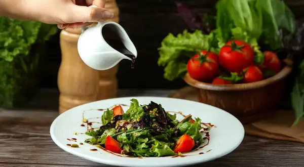 Ein Salat wird mit Balsamico beträufelt. Balsamico besteht aus eingekochtem Traubenmost, Essig und oft weiteren Zutaten.