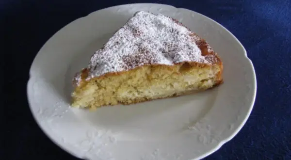 Ein Stück saftiger irischer Apfelkuchen, bestäubt mit Puderzucker, auf einem weißen Teller.