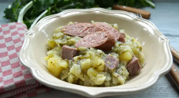 Herzhaftes Stielmus mit Kartoffeln und Wurst in einer Schüssel, daneben ein kariertes Tuch.