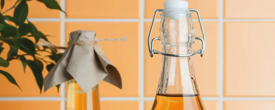 Zwei Flaschen mit bernsteinfarbener Flüssigkeit, eine mit Bügelverschluss, die andere mit Papier und Schnur abgedeckt. Essig oder Essigessenz für die Küche.