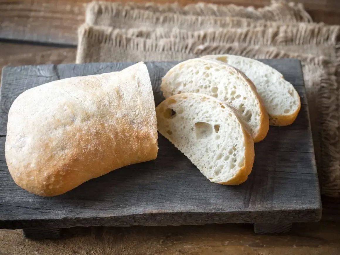Ein rustikales ciabatta mit sauerteig, aufgeschnitten auf einem Holzbrett.
