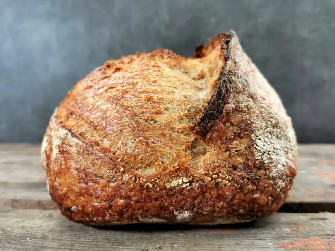 Ein rustikales Brot mit knuspriger Kruste und luftiger brot krume liegt auf Holzbrettern.