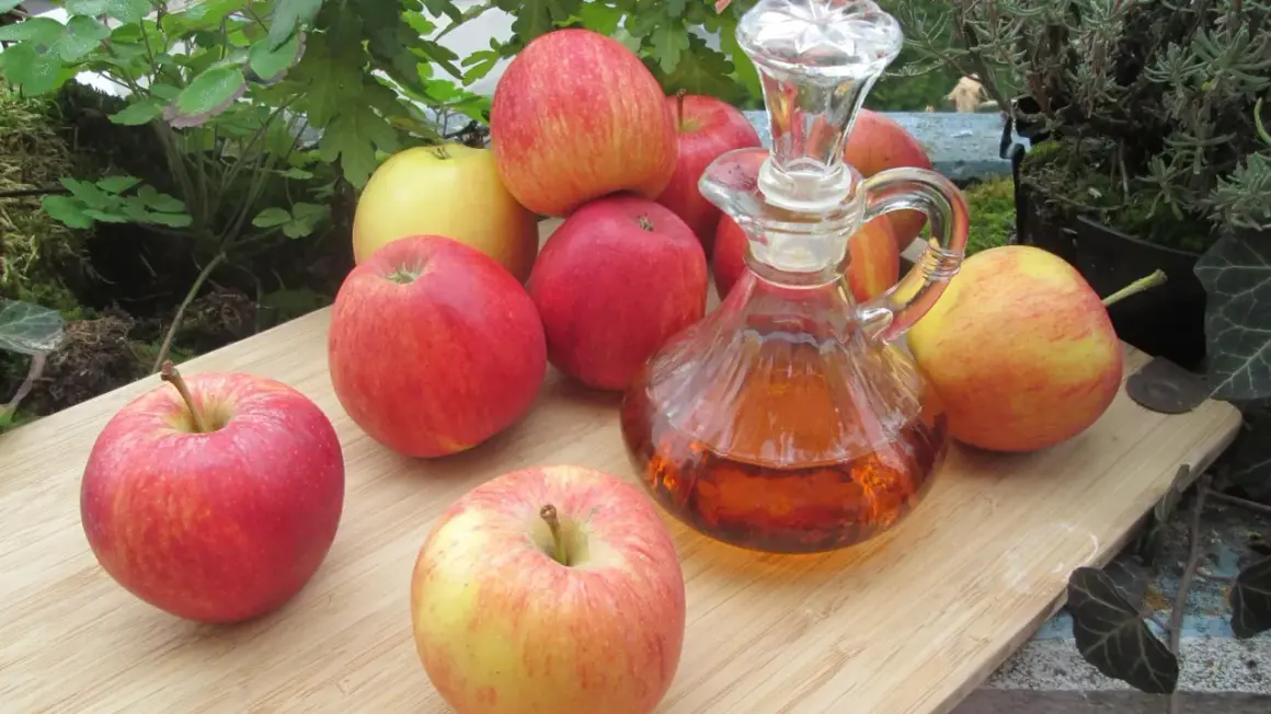 Frische Äpfel und eine Karaffe mit bernsteinfarbenem Apfelessig – eine natürliche obstessig alternative für Küche und Gesundheit.