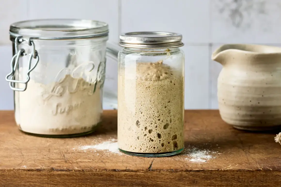 Ein Glas mit aktivem Sauerteig, bereit zum Anstellgut auffrischen. Daneben ein Glas mit Mehl und eine Kanne.