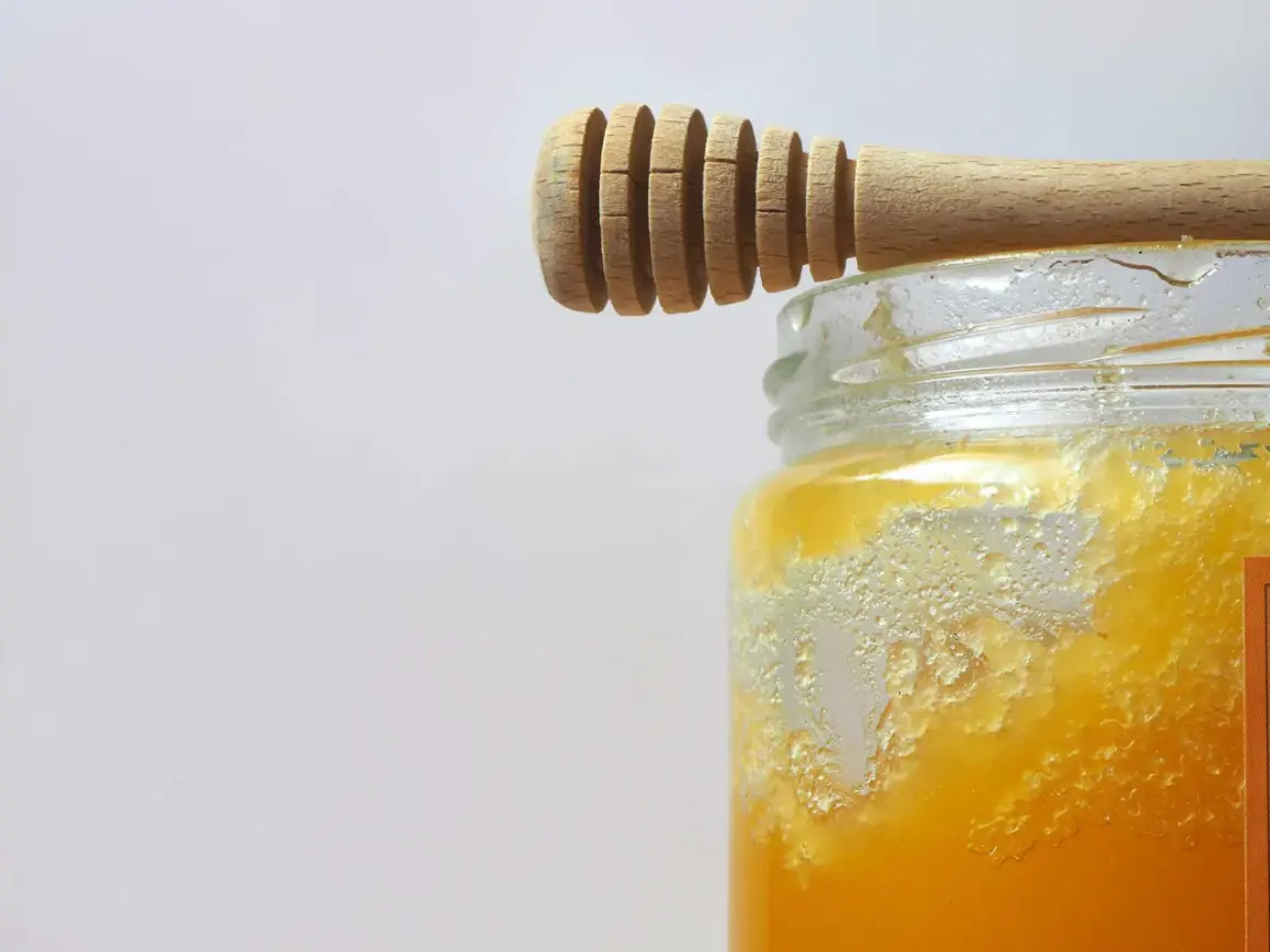 Ein Holzlöffel ruht auf einem Glas mit honig kristallisiert. Die Kristalle bilden eine interessante Textur.