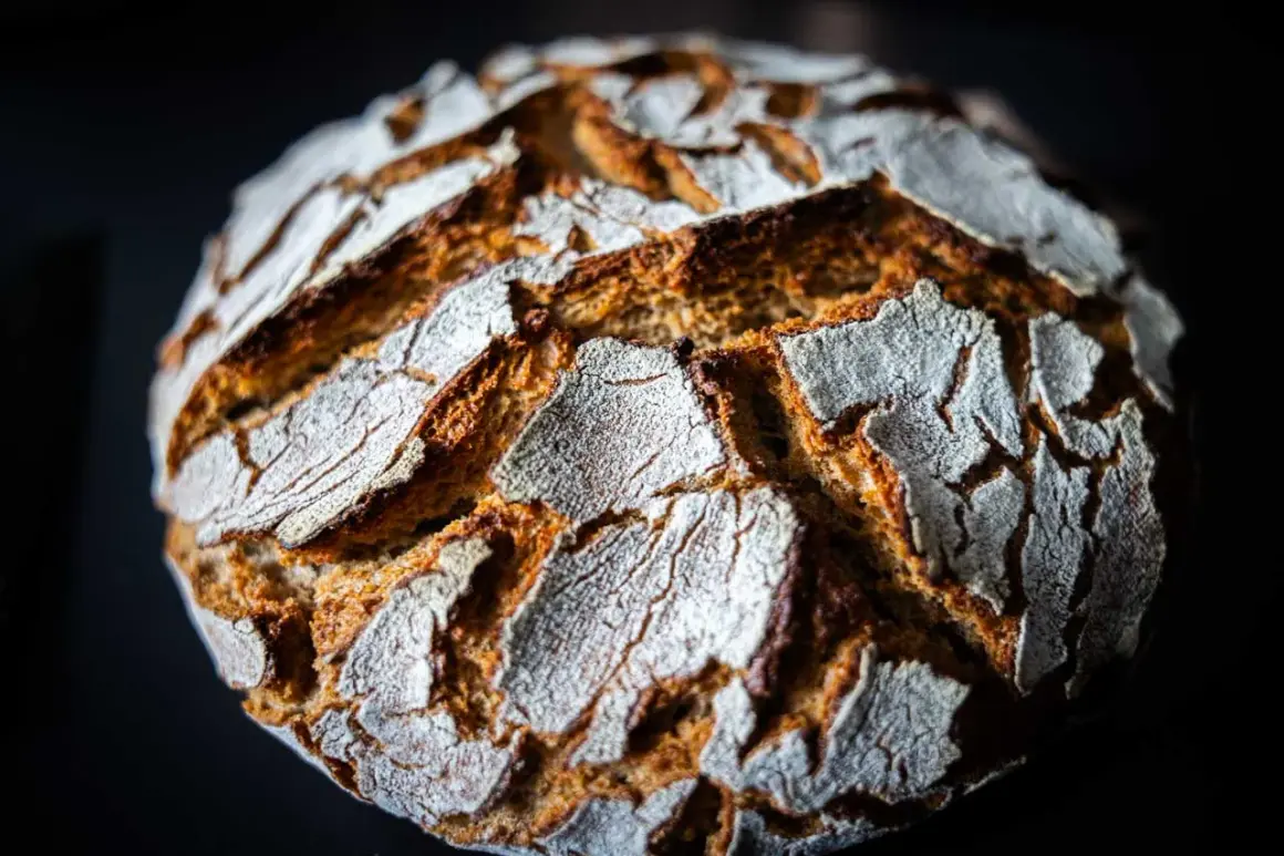 Ein rustikales Roggenmischbrot mit Sauerteig, dessen Kruste mit Mehl bestäubt ist und tiefe Rillen aufweist.