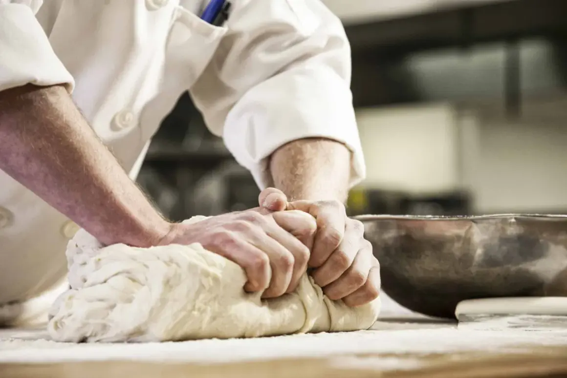 Hände kneten kräftig Brotteig. Die Frage "wie lange brotteig kneten" beschäftigt Bäcker, um das perfekte Ergebnis zu erzielen.