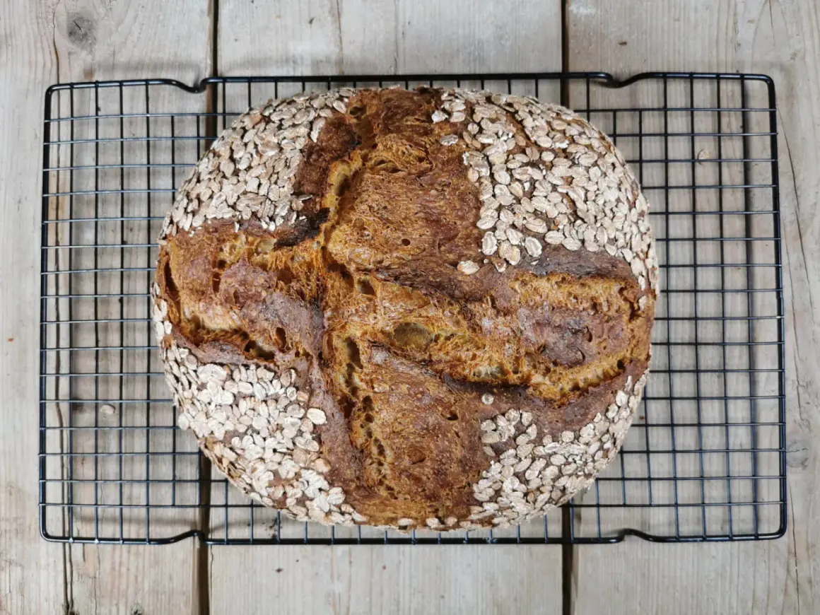 Ein rustikales Porridge Brot mit Haferflockenkruste, das auf einem Gitterrost abkühlt.